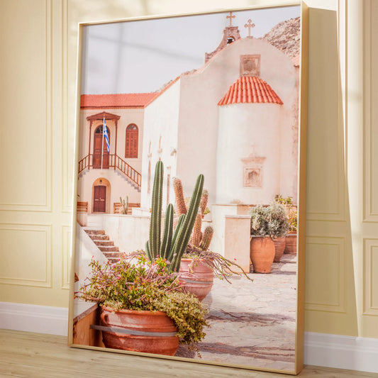 テラコッタ鉢のサボテンと花に囲まれた、白壁とオレンジ色の屋根瓦が特徴的なギリシャ正教会。階段と木製扉、ギリシャ国旗が印象的な地中海建築の風景。