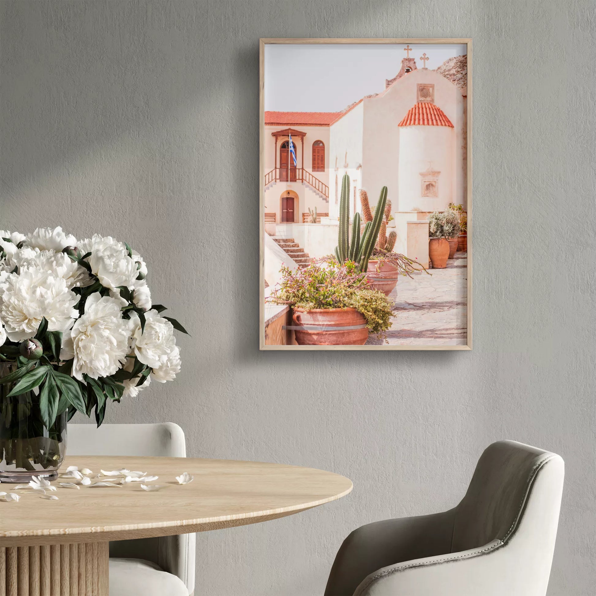 テラコッタ鉢のサボテンと花に囲まれた、白壁とオレンジ色の屋根瓦が特徴的なギリシャ正教会。階段と木製扉、ギリシャ国旗が印象的な地中海建築の風景。