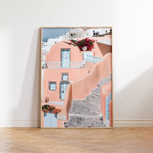 サントリーニ島のパステルピンクの建物と水色のドア、赤いブーゲンビリアが咲く地中海建築アート。白壁の街並みと石畳の小道が見える風景。