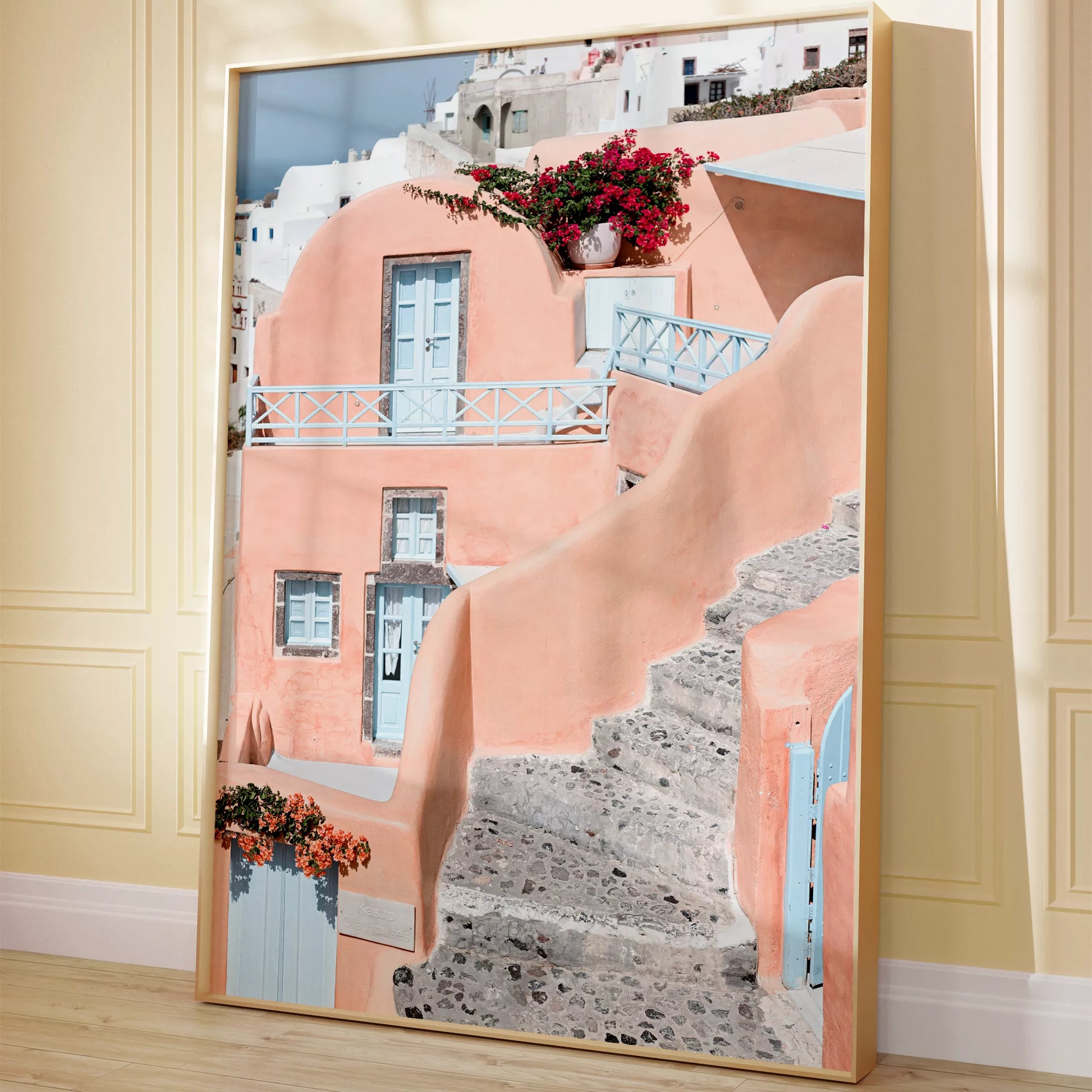 サントリーニ島のパステルピンクの建物と水色のドア、赤いブーゲンビリアが咲く地中海建築アート。白壁の街並みと石畳の小道が見える風景。