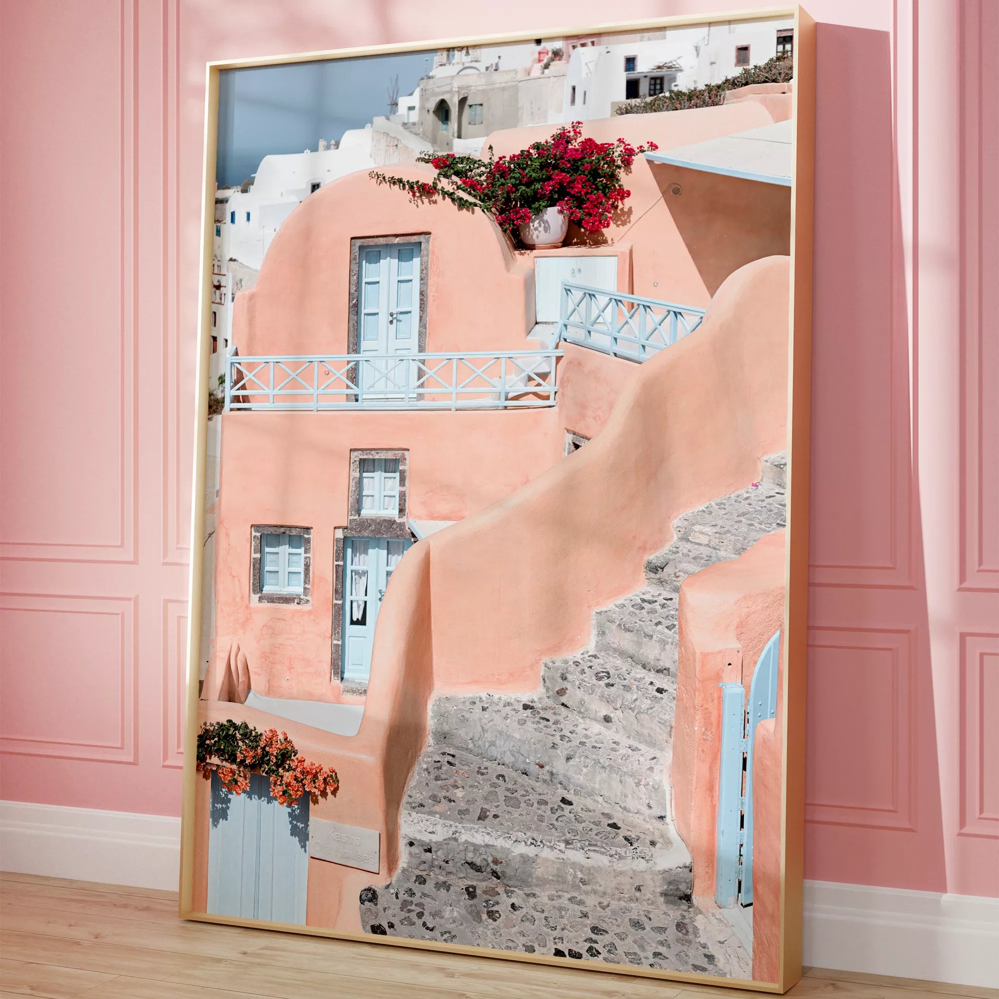 サントリーニ島のパステルピンクの建物と水色のドア、赤いブーゲンビリアが咲く地中海建築アート。白壁の街並みと石畳の小道が見える風景。