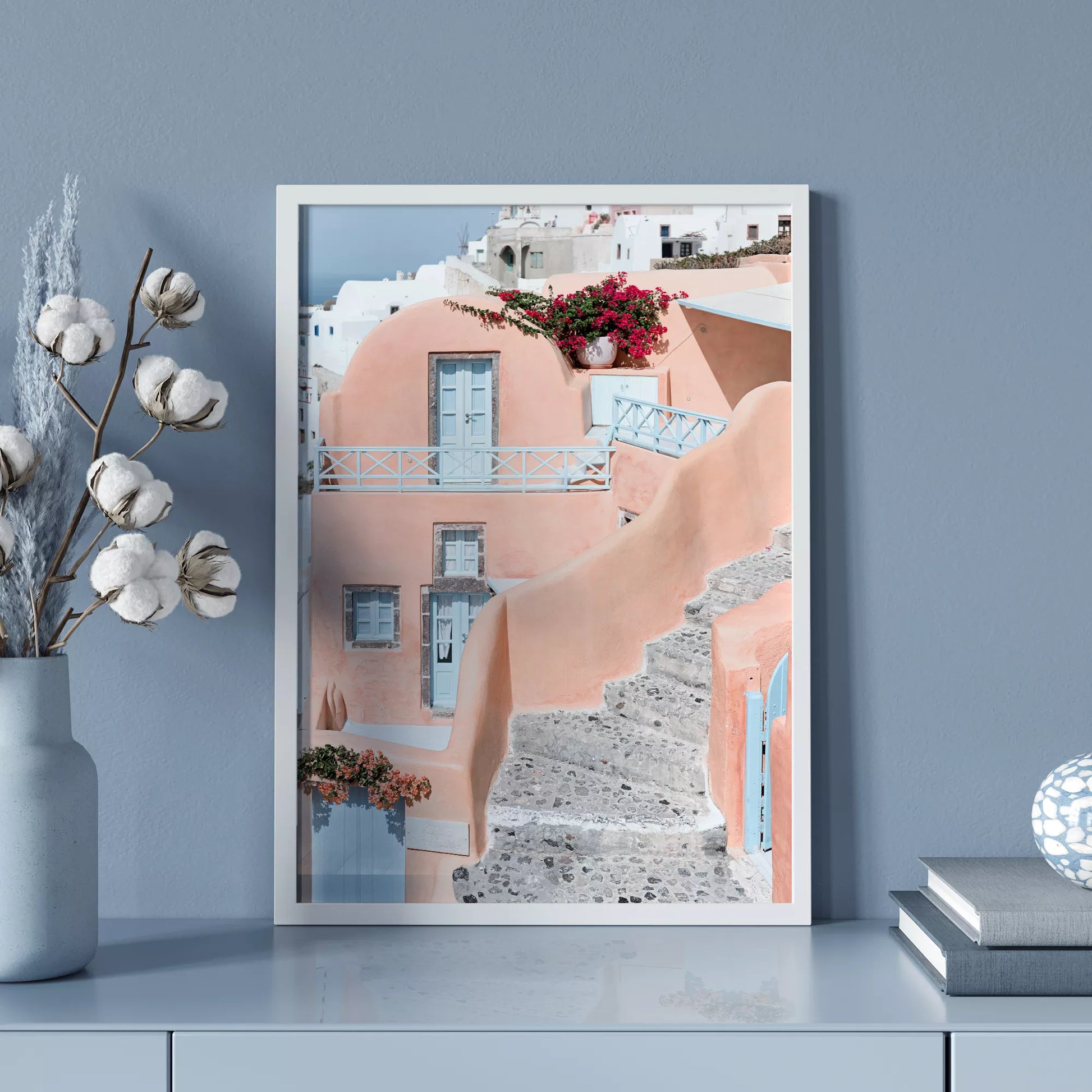 サントリーニ島のパステルピンクの建物と水色のドア、赤いブーゲンビリアが咲く地中海建築アート。白壁の街並みと石畳の小道が見える風景。