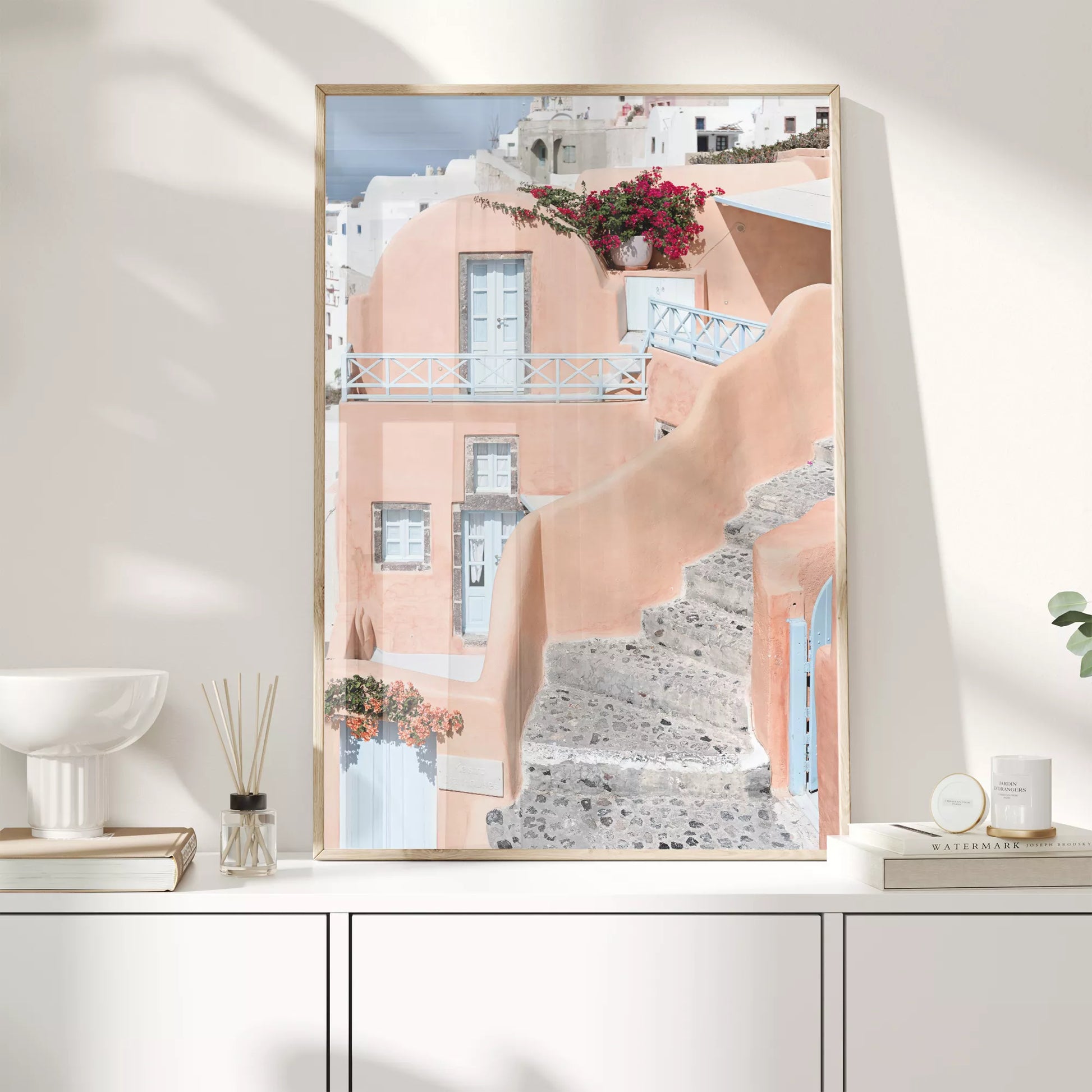 サントリーニ島のパステルピンクの建物と水色のドア、赤いブーゲンビリアが咲く地中海建築アート。白壁の街並みと石畳の小道が見える風景。