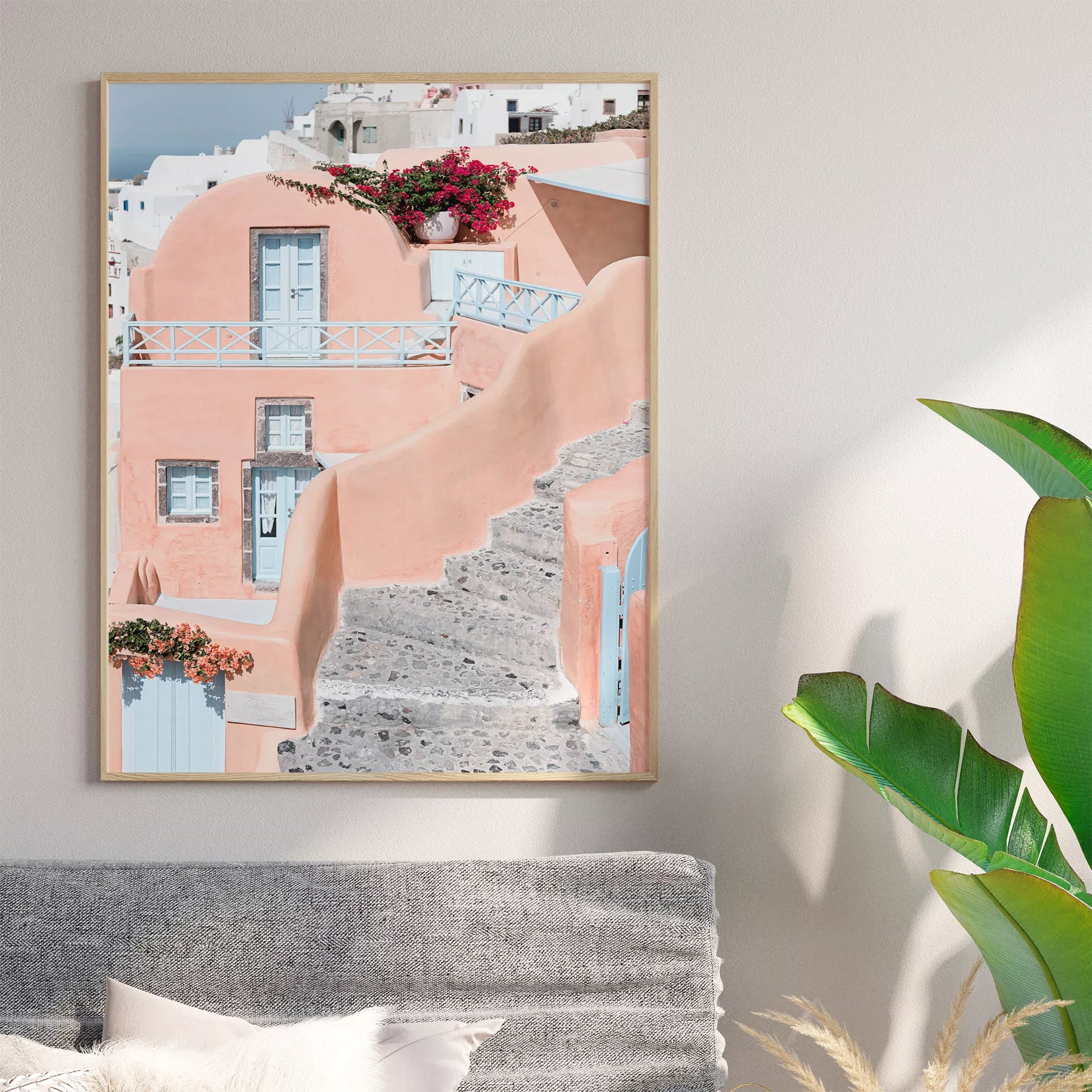 サントリーニ島のパステルピンクの建物と水色のドア、赤いブーゲンビリアが咲く地中海建築アート。白壁の街並みと石畳の小道が見える風景。