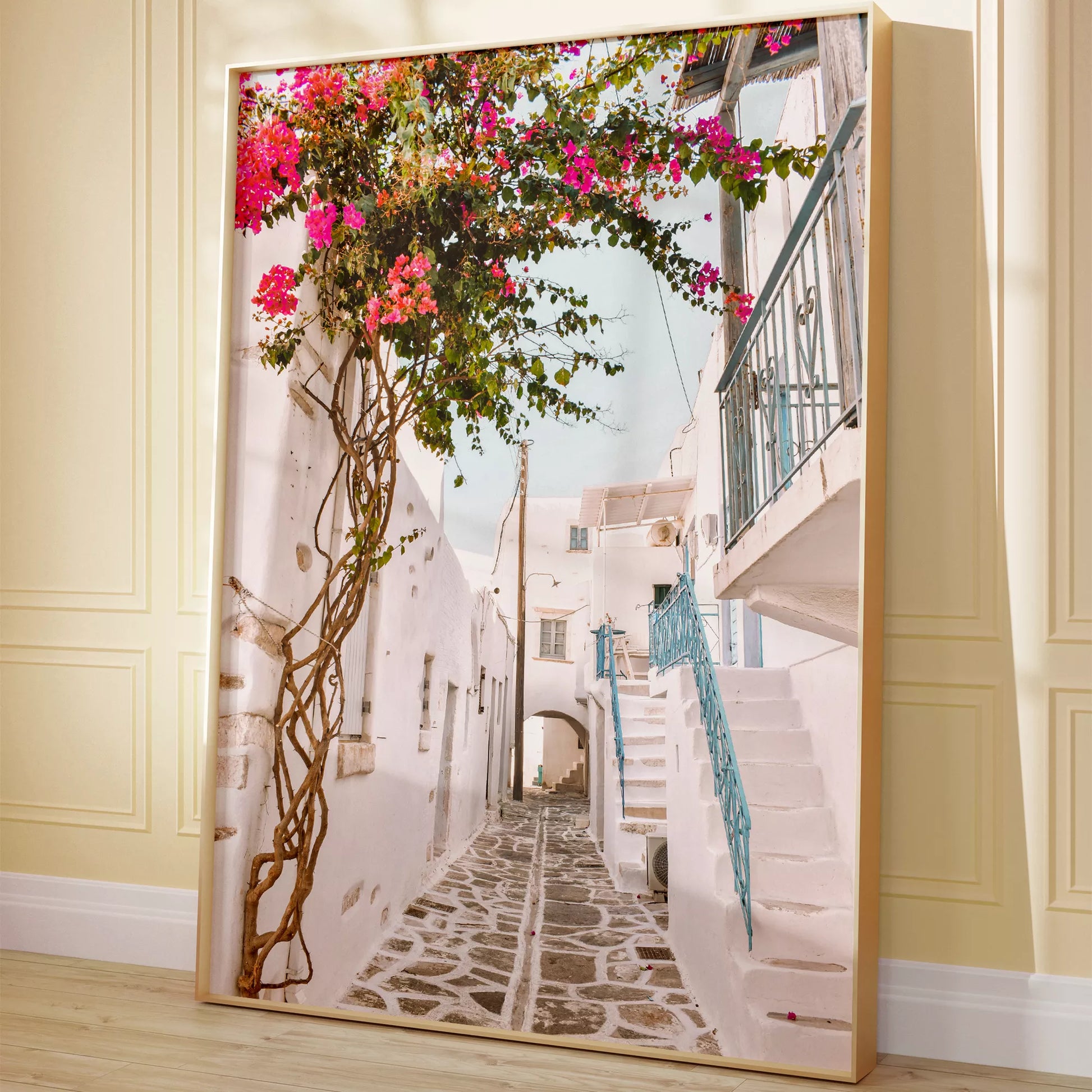 白壁の建物が並ぶ石畳の小道に、鮮やかなピンクのブーゲンビリアが咲き誇り、青い手すりの階段が印象的な地中海風の街並み。伝統的なキクラデス建築と自然が調和した魅力的な景観。