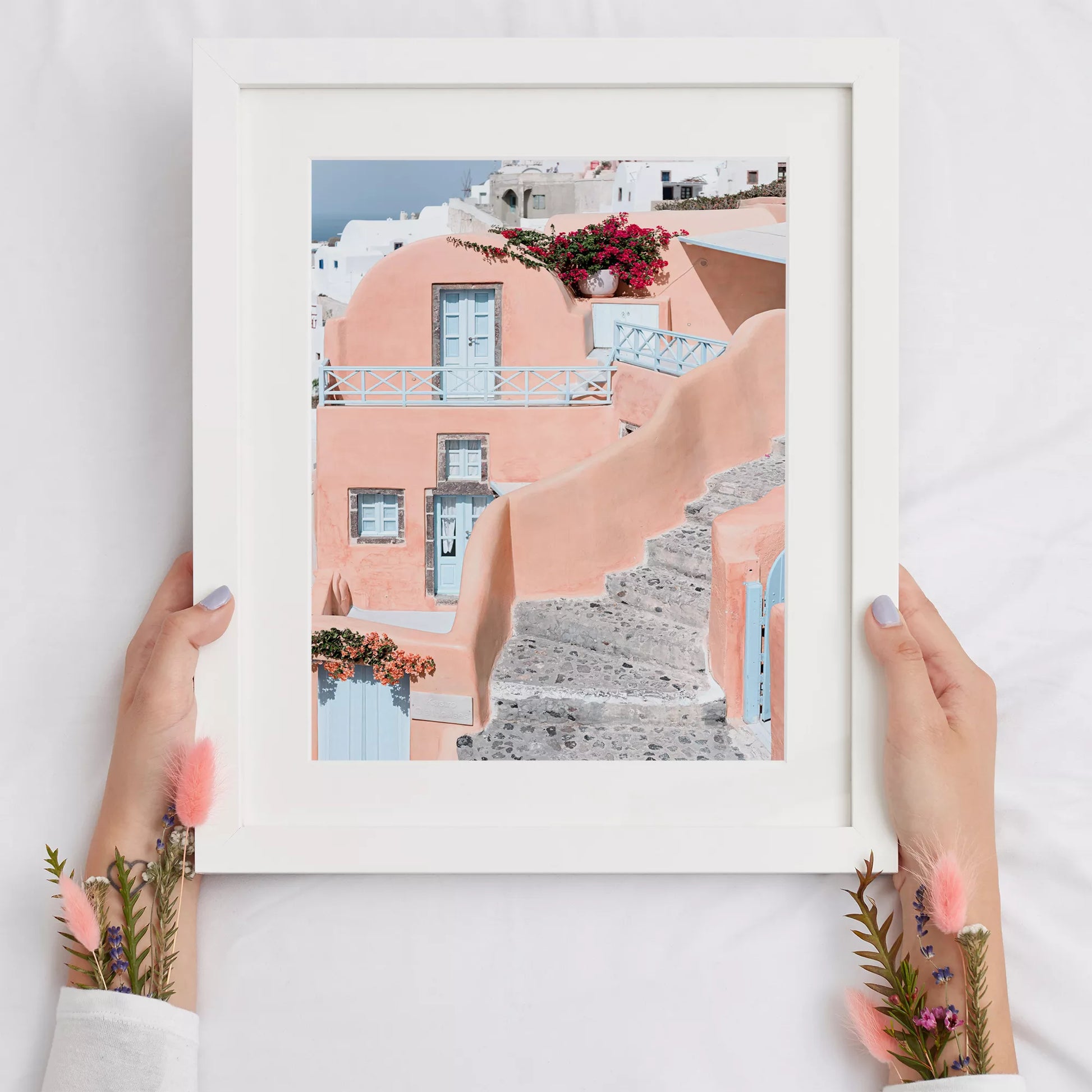 サントリーニ島のパステルピンクの建物と水色のドア、赤いブーゲンビリアが咲く地中海建築アート。白壁の街並みと石畳の小道が見える風景。