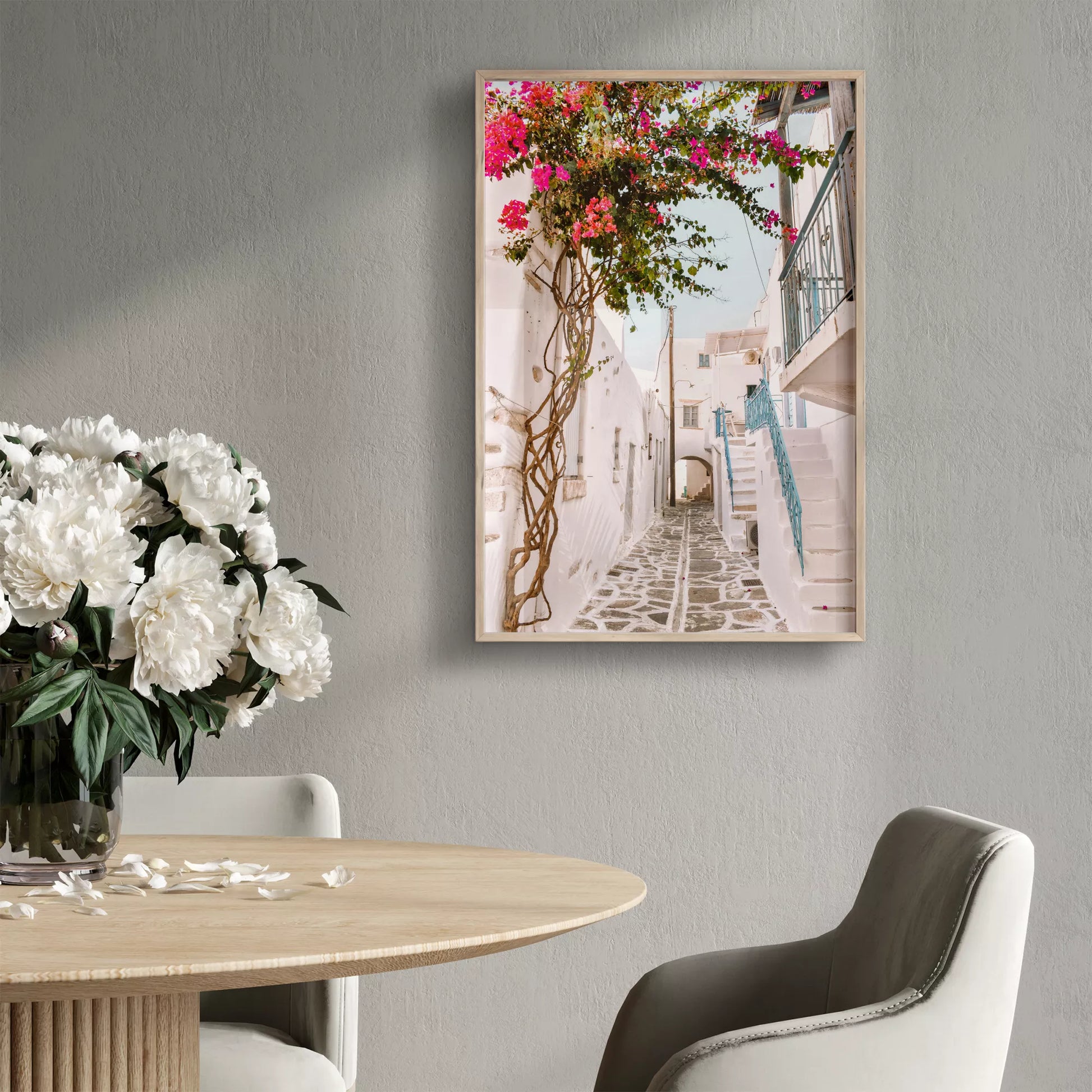 白壁の建物が並ぶ石畳の小道に、鮮やかなピンクのブーゲンビリアが咲き誇り、青い手すりの階段が印象的な地中海風の街並み。伝統的なキクラデス建築と自然が調和した魅力的な景観。