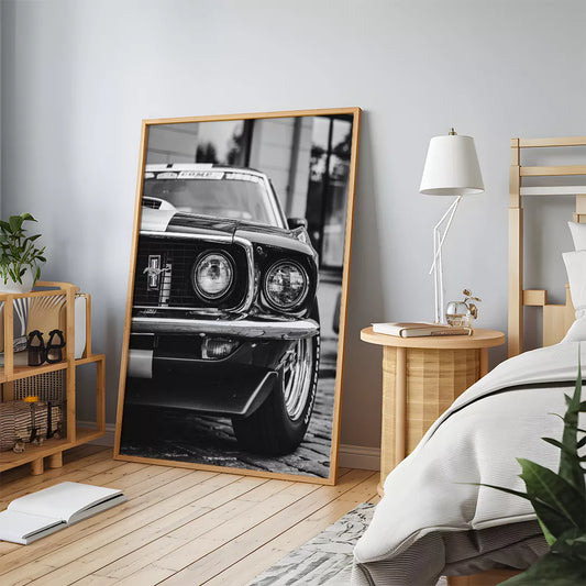 クラシックマスタングのフロントビューを捉えたモノクロ写真。象徴的な馬のエンブレムとデュアルヘッドライトが特徴的で、車体の光沢感と細部のディテールが際立つアーティスティックなショット。