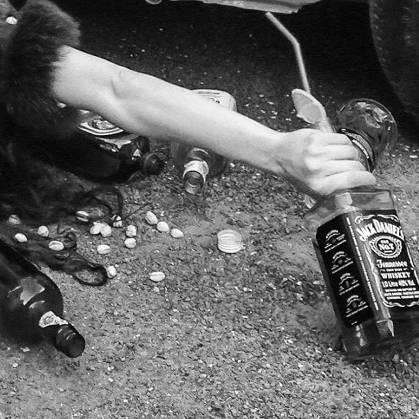 Black and white photograph of a person lying amidst alcohol bottles