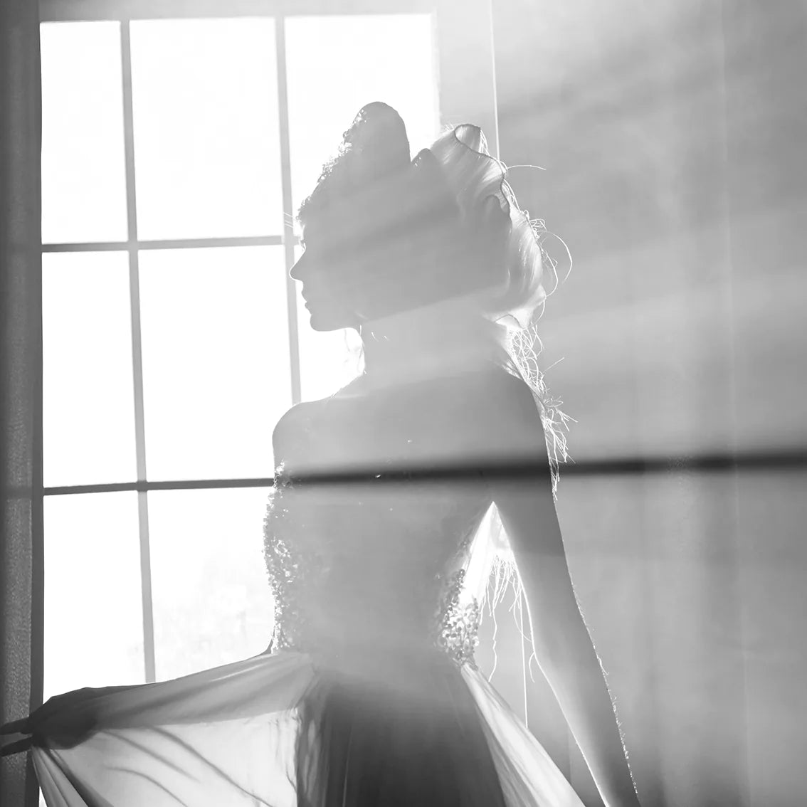 Elegant bride standing by the window, her wedding gown illuminated in the soft light