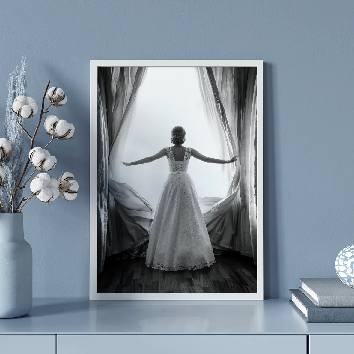 Black and white image of a bride in a lace wedding dress standing at an open window