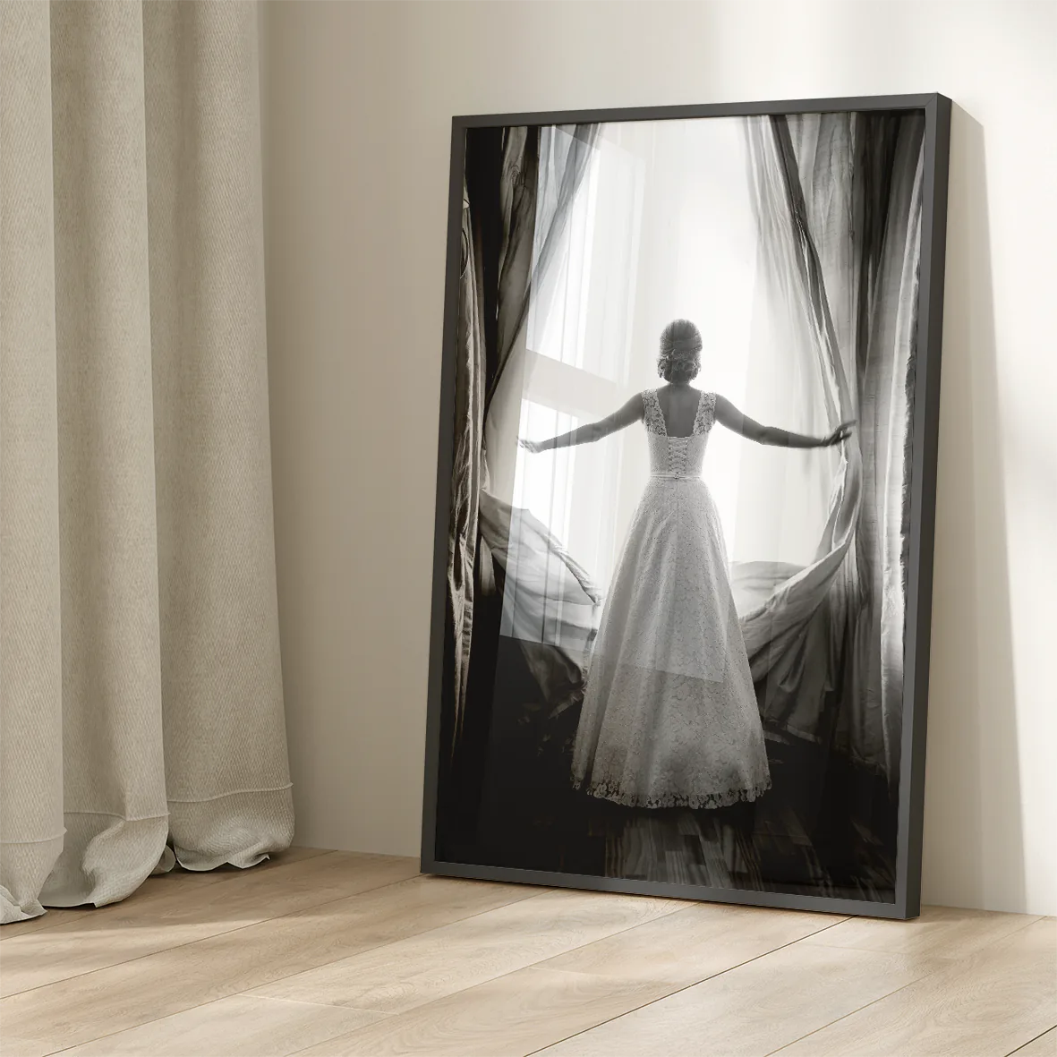 Black and white image of a bride in a lace wedding dress standing at an open window