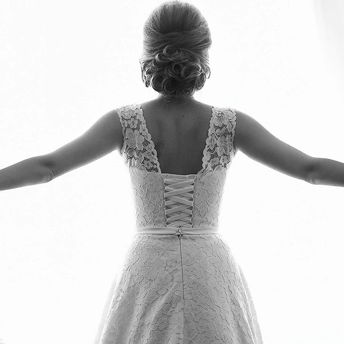 Black and white image of a bride in a lace wedding dress standing at an open window