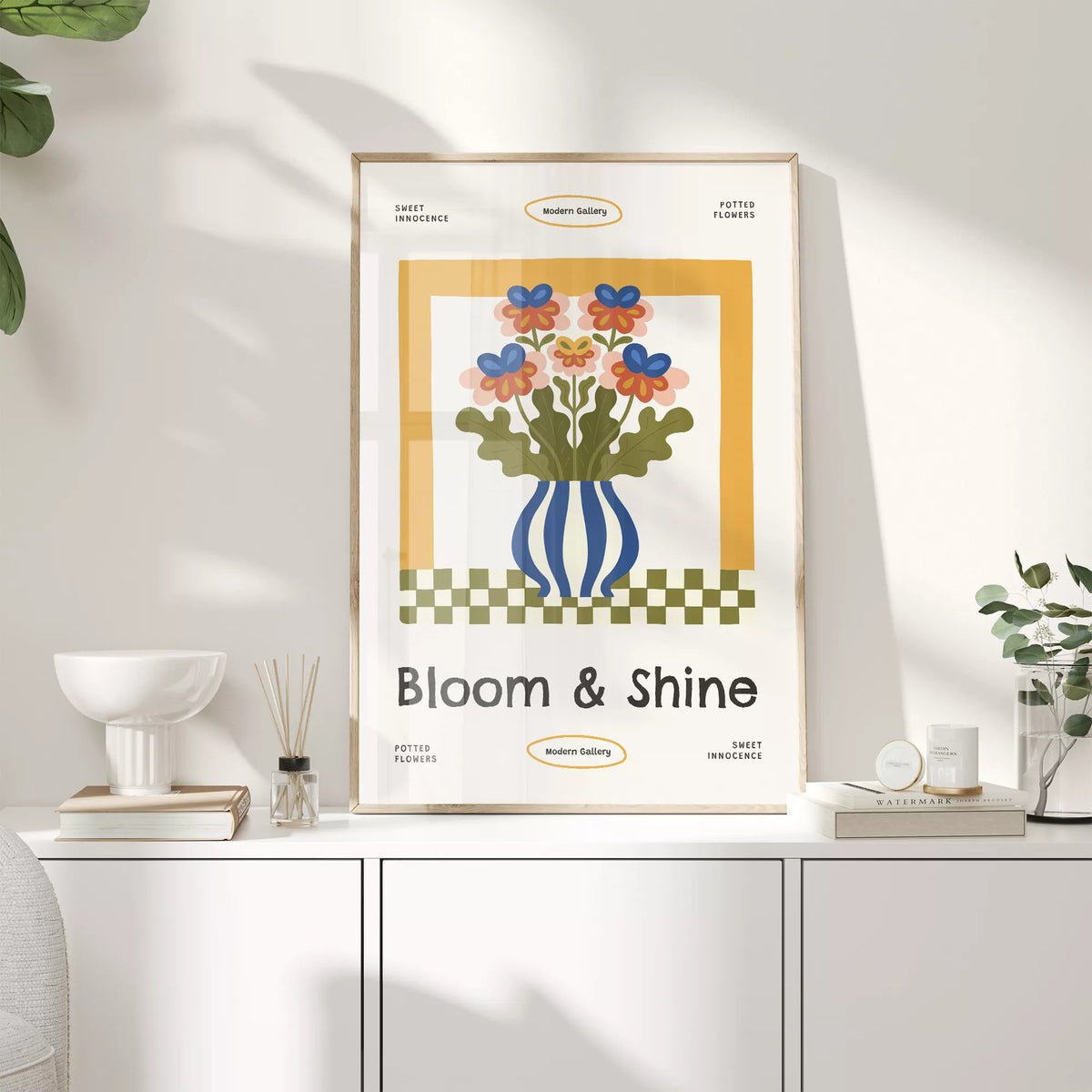 白いキャビネットの上に置いた、カラフルな花とBloom & Shineの文字入りポスター
