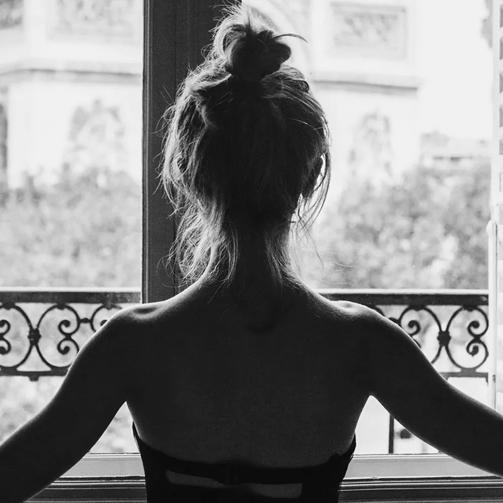 まとめ髪の女性の後ろ姿と、窓の外に広がるパリの景色を写した白黒写真のクローズアップ