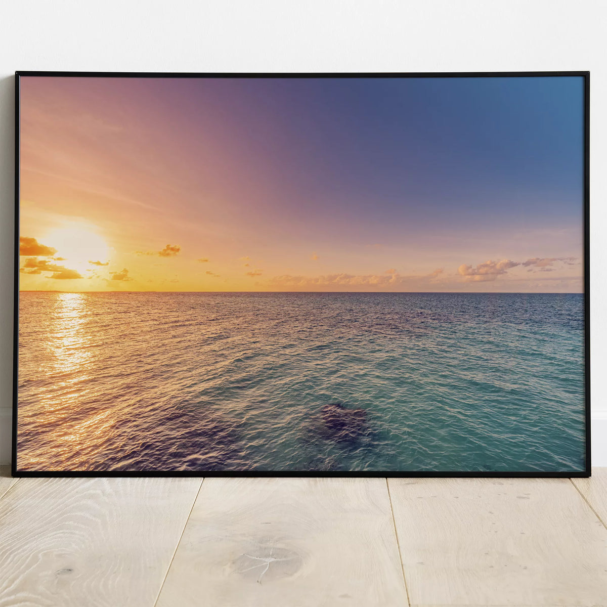 白い壁と木の床に立てかけた、オレンジの夕日がきらめく海の横長ポスター