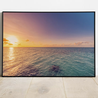 白い壁と木の床に立てかけた、オレンジの夕日がきらめく海の横長ポスター