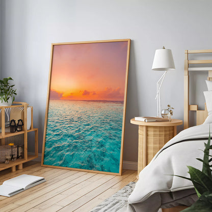木製家具のある寝室の床に立て掛けた、ターコイズの海と夕空の縦長ポスター